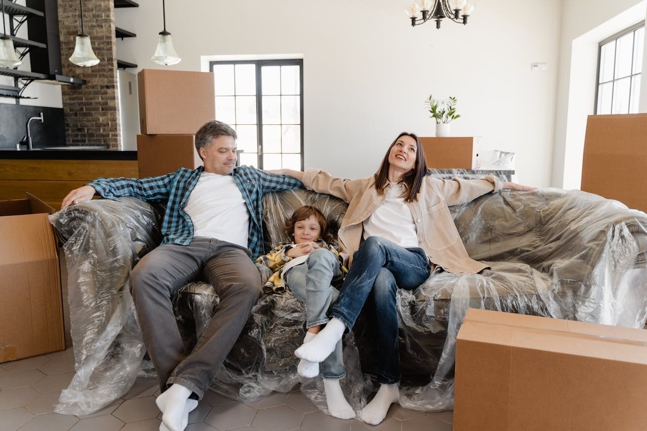 Happy family sitting on a couch with cardboard boxes all around the living room.